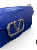 SWORD LUXURY Valentino Garavani VLogo Signature mavi Ayers deri çanta, taşlı VLogo amblemi ve zincir askı detayı.