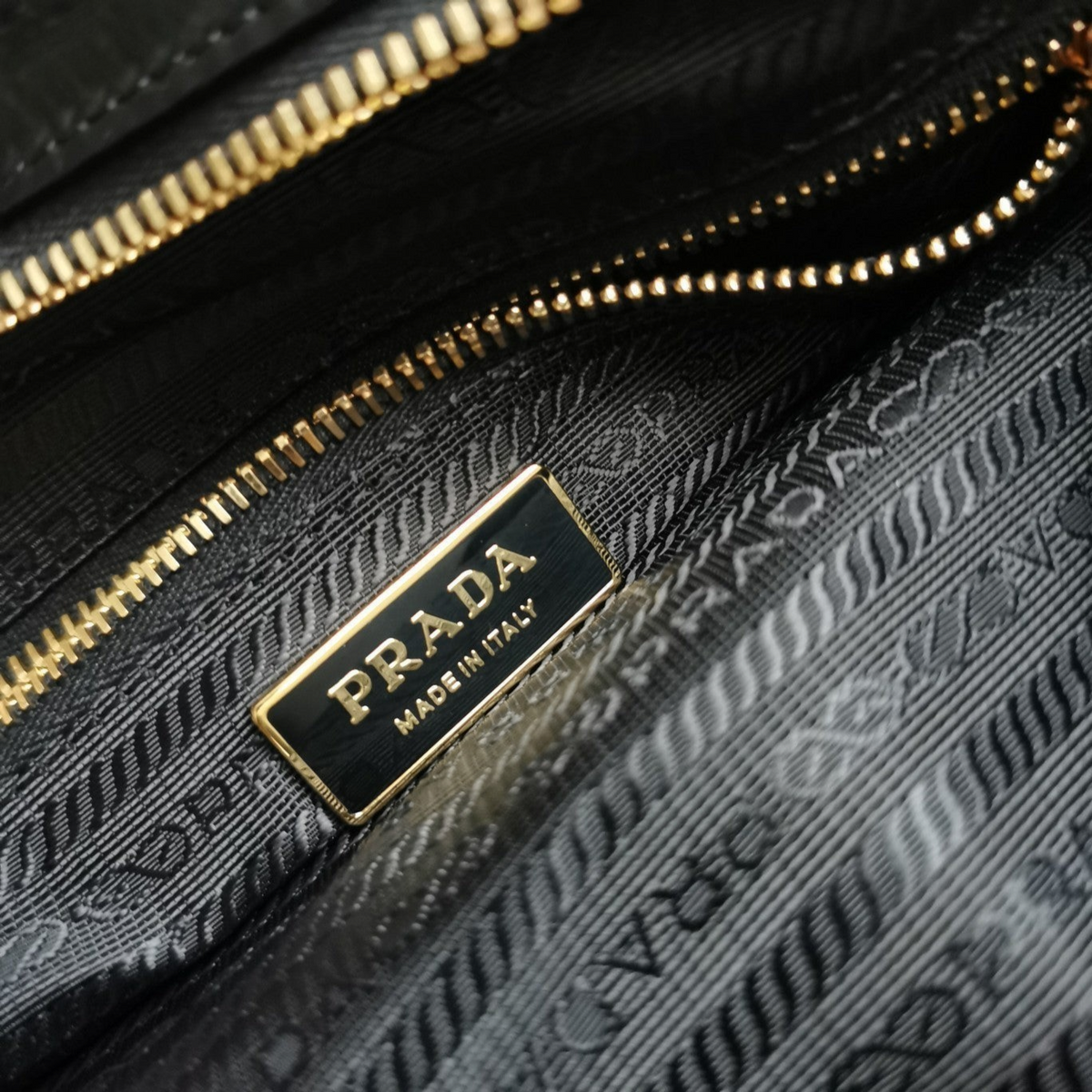 SWORD LUXURY Prada Bonnie çanta içi detayları, altın tonlu logo plakası ve fermuarlı bölme ile siyah astar.