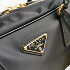 SWORD LUXURY Prada Re-Nylon ve Saffiano deri detaylı siyah çanta, altın tonlu üçgen logo ve fermuar detaylı.