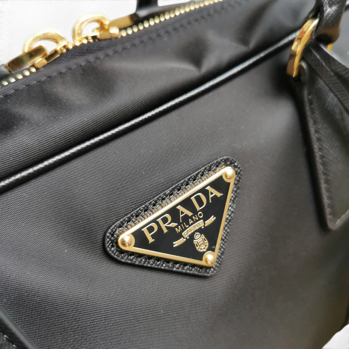 SWORD LUXURY Prada Re-Nylon ve Saffiano deri detaylı siyah çanta, altın tonlu üçgen logo ve fermuar detaylı.
