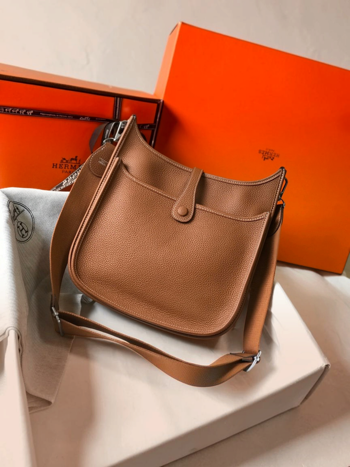 SWORD LUXURY taba rengi deri Hermès Evelyne PM 28 çanta, ayarlanabilir kanvas askı ve ikonik H logolu tasarım.