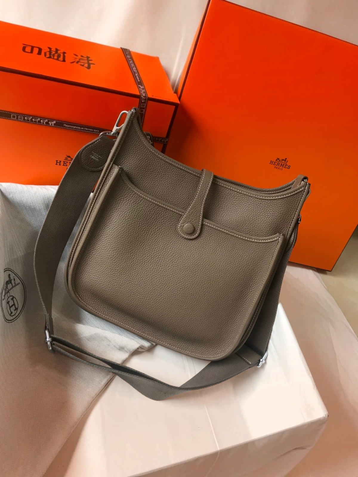 SWORD LUXURY marka, taupe renkli, delikli H logolu, ayarlanabilir kanvas askılı deri Hermès Evelyne PM 28 çanta.