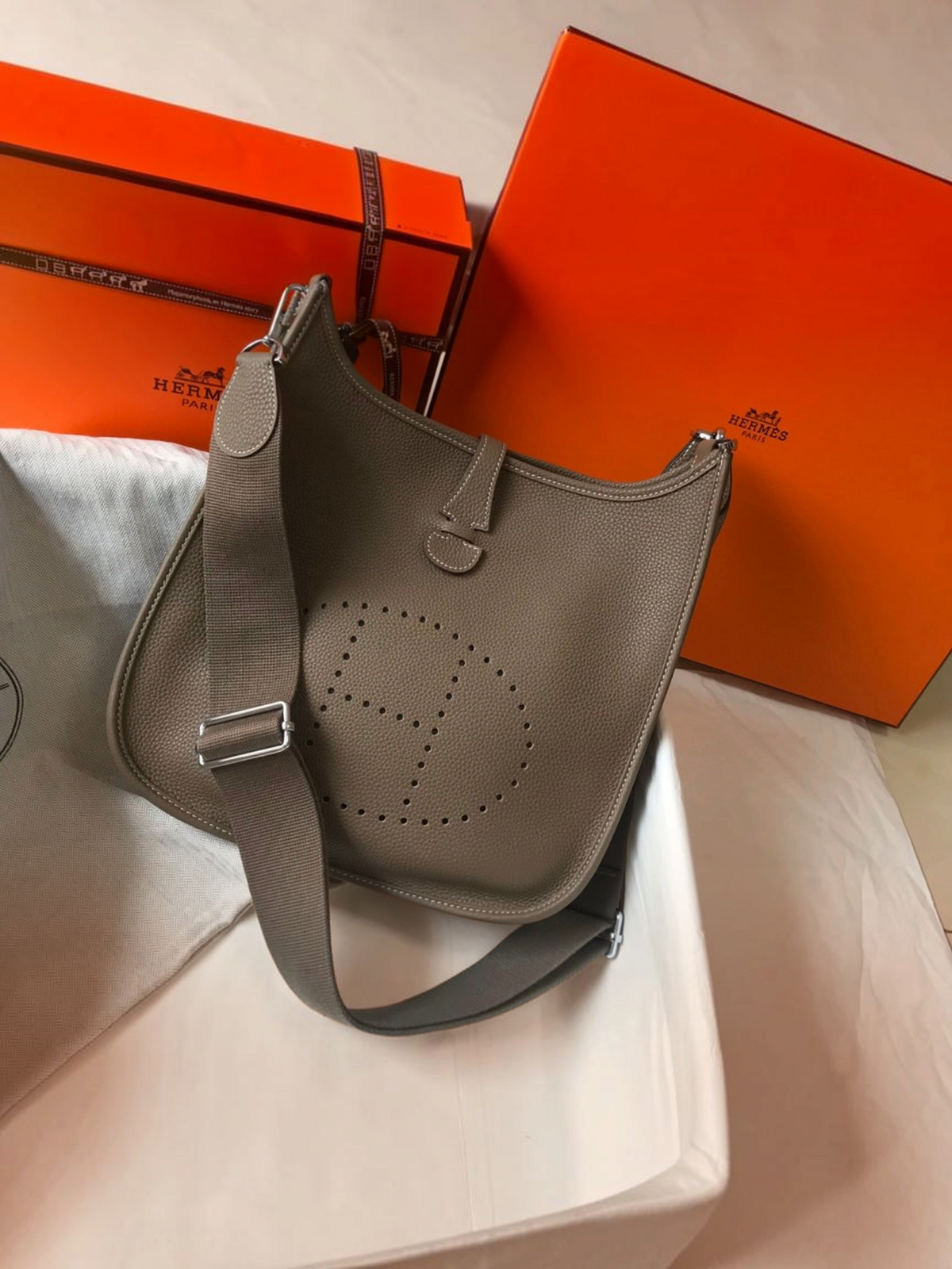 SWORD LUXURY Hermès Evelyne PM 28 gri renkli, delikli H logolu ve ayarlanabilir kanvas askılı deri çanta.