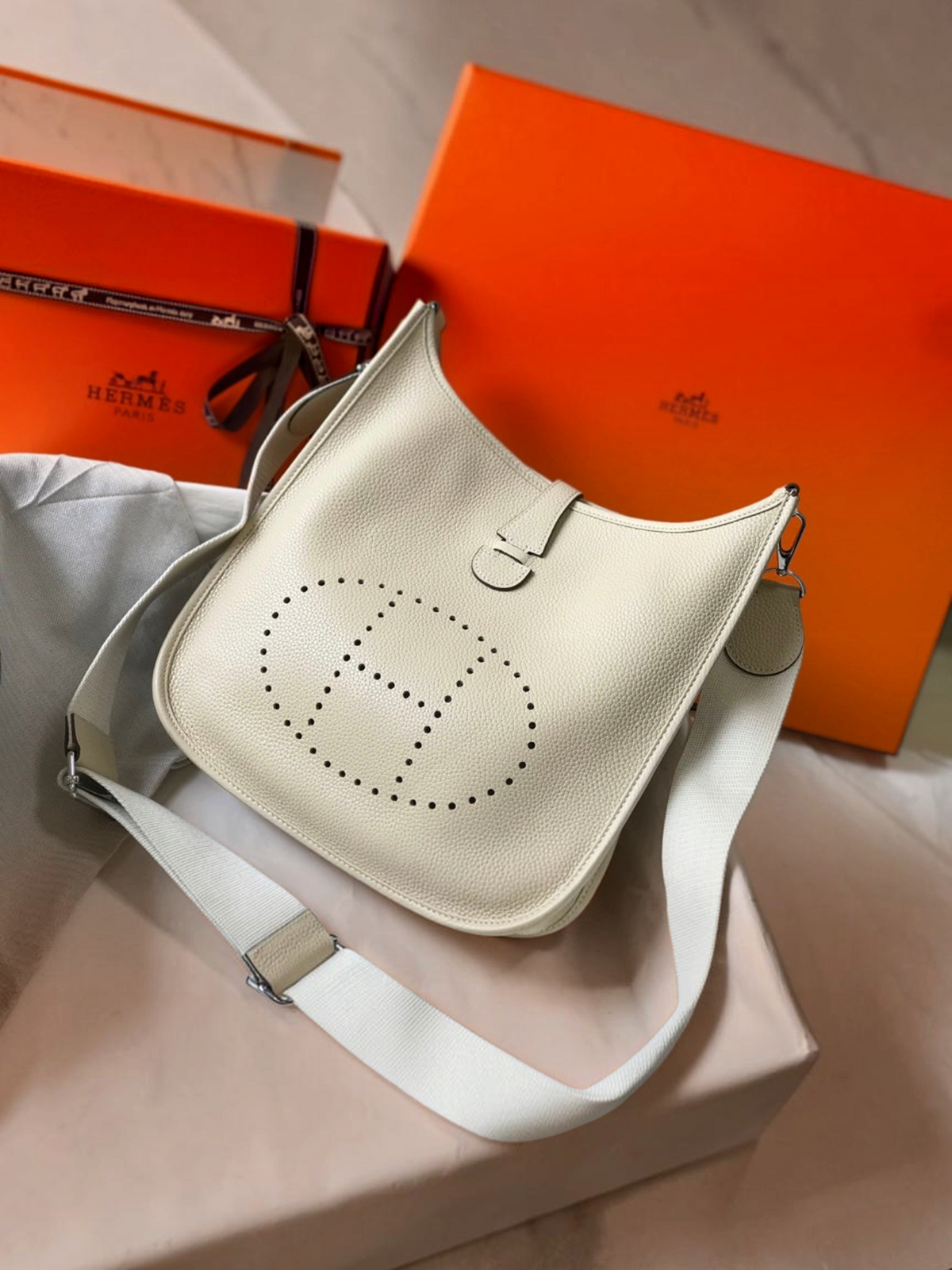 SWORD LUXURY imzalı, bej renkli, delikli H logolu ve ayarlanabilir kanvas askılı deri Hermès Evelyne PM 28 çanta.