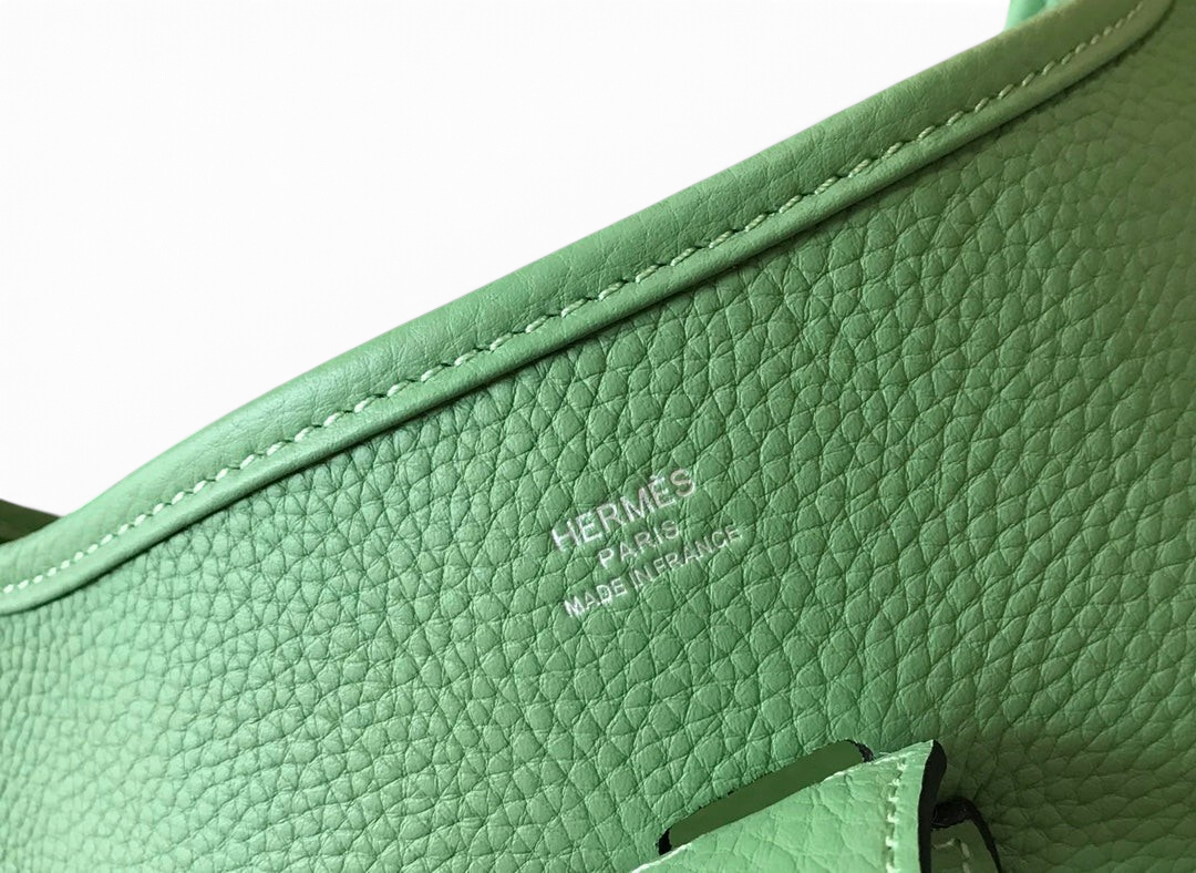 SWORD LUXURY Hermès Evelyne PM 28 çanta, yeşil damarlı deri detayları ve gümüş kabartmalı logo baskısı ile.