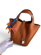 SWORD LUXURY taba rengi Clemence deri Hermès Picotin 18 çanta, gümüş asma kilit ve renkli at figürlü çanta süsü ile.