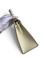 SWORD LUXURY marka, beyaz Epsom deri Kelly 25 çanta, yan görünüm, gümüş donanım ve beyaz eldivenli el ile tutuluyor.