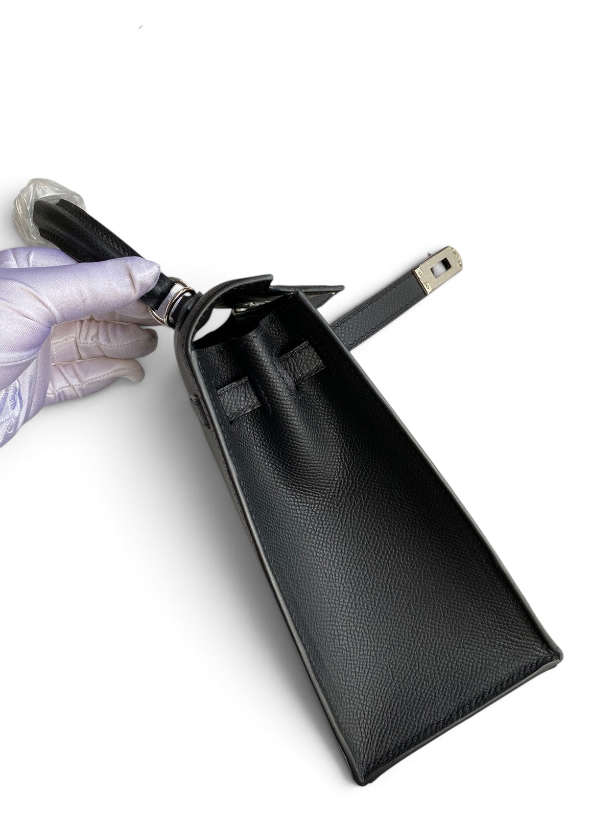 SWORD LUXURY siyah Epsom deri Kelly 25 çanta, gümüş tonlu donanım ve eldivenli elle tutulan yan profil görünümü.
