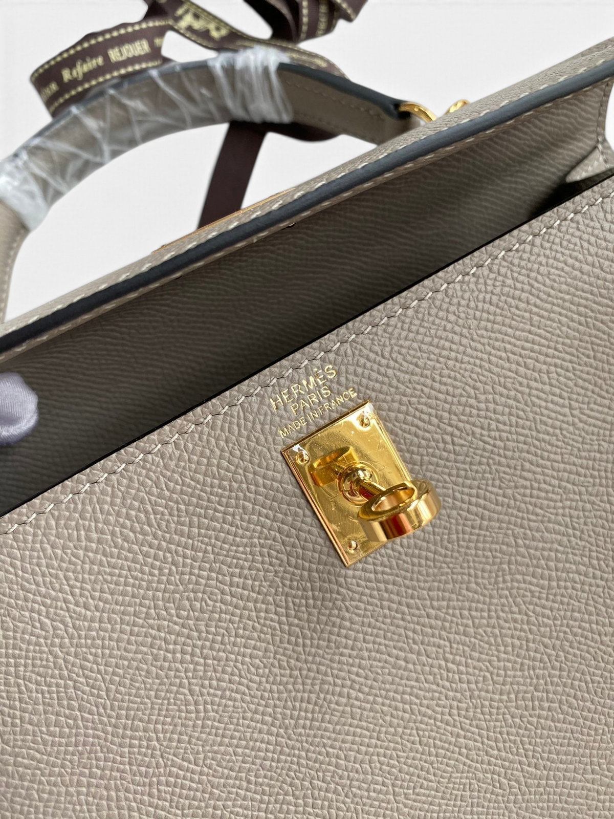 SWORD LUXURY marka gri Epsom deri Kelly 25 çanta, altın tonlu donanım ve ikonik kilit detayı ile.