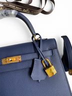 SWORD LUXURY lacivert Epsom deri Hermès Kelly 25 çanta, altın tonlu donanım, kilit ve anahtarlı clochette detaylı.