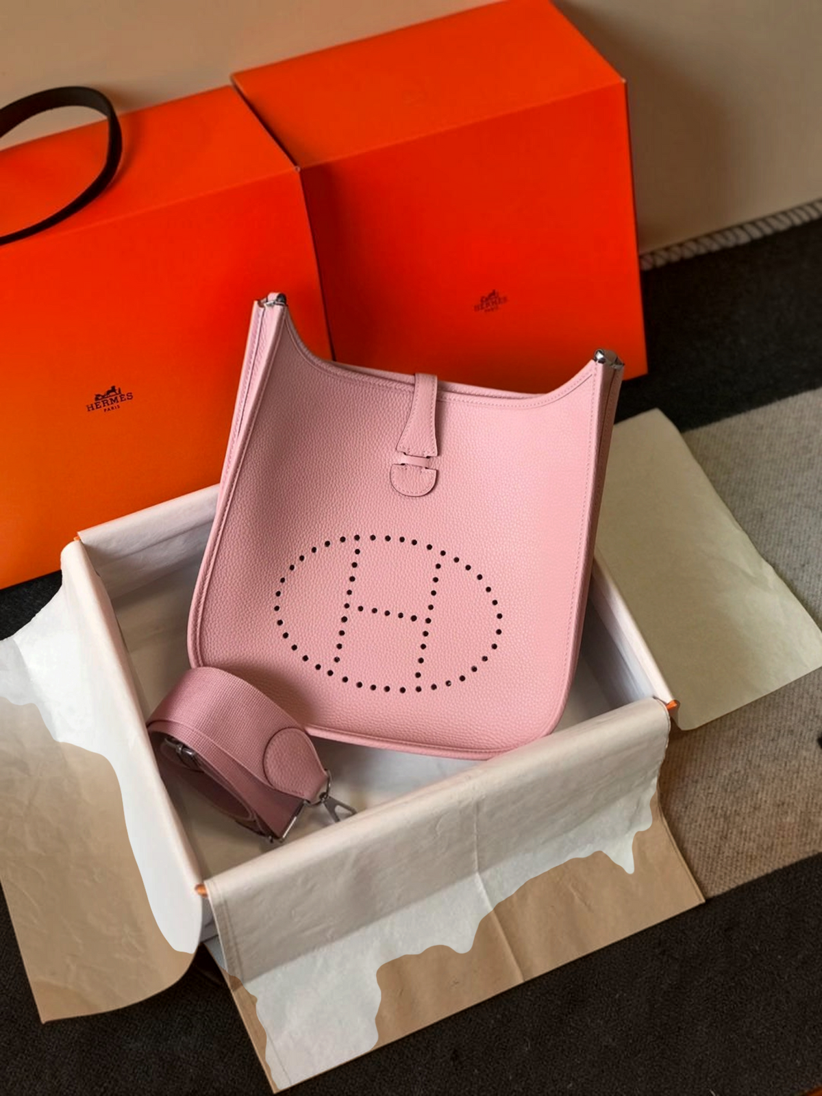 SWORD LUXURY pembe deri Hermès Evelyne PM 28 çanta, ön yüzünde ikonik delikli H logosu ve ayarlanabilir kanvas askı.