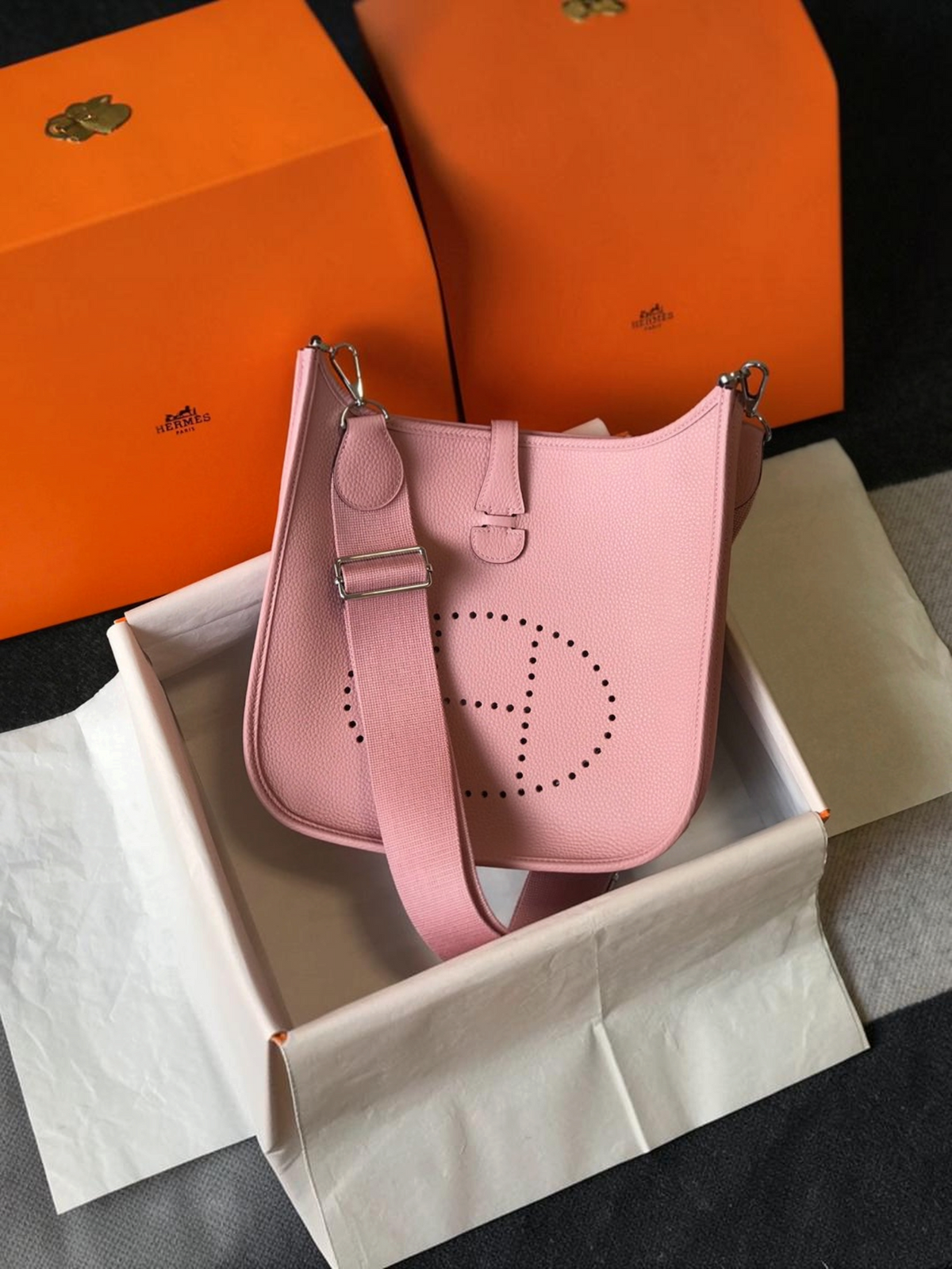 SWORD LUXURY pembe deri Hermès Evelyne PM 28 çanta, ön yüzünde delikli H logosu ve ayarlanabilir kanvas askı ile.