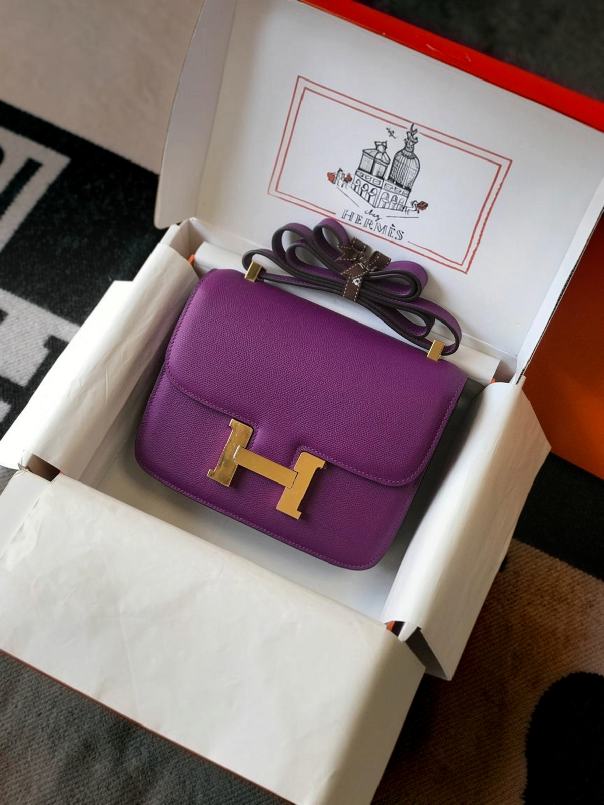 SWORD LUXURY marka, altın H tokalı, mor deri Hermès Constance 18 çanta, orijinal kutusunda sergileniyor.