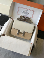 SWORD LUXURY marka krem rengi deri Hermès Constance 18 çanta, gümüş tonlu H tokasıyla kutusunda sergileniyor.