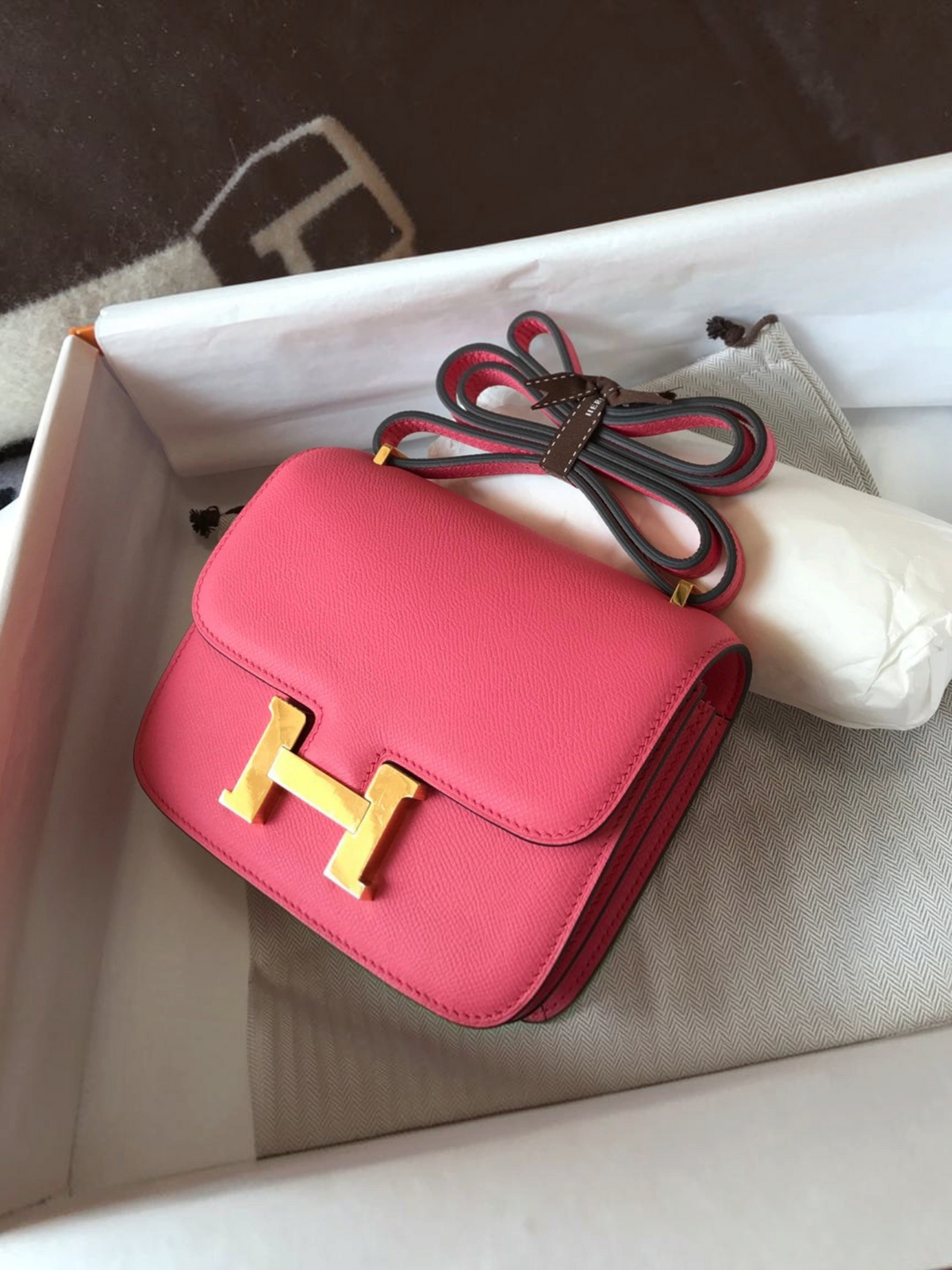 SWORD LUXURY Hermès Constance 18 çanta, altın tonlu H tokalı gül pembesi deri tasarım, kutu içerisinde sergileniyor.