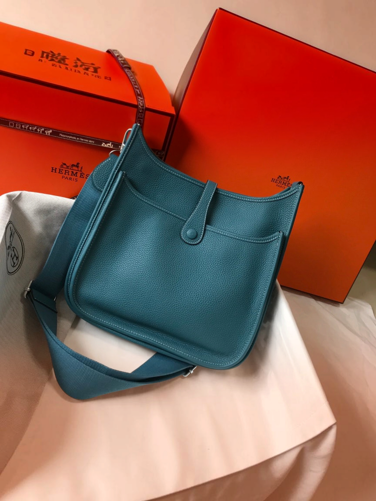 SWORD LUXURY marka, turkuaz renkli, delikli H logolu ve ayarlanabilir kanvas askılı deri Hermès Evelyne PM 28 çanta.