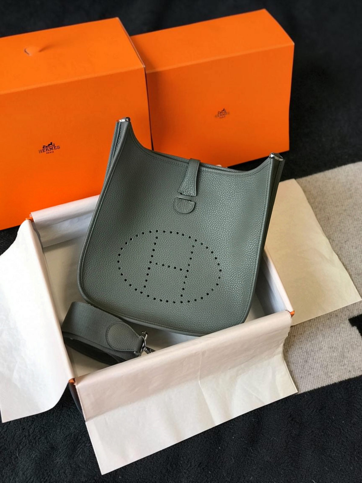 SWORD LUXURY Hermès Evelyne PM 28 gri renkli, delikli H logolu ve ayarlanabilir kanvas askılı deri çanta.