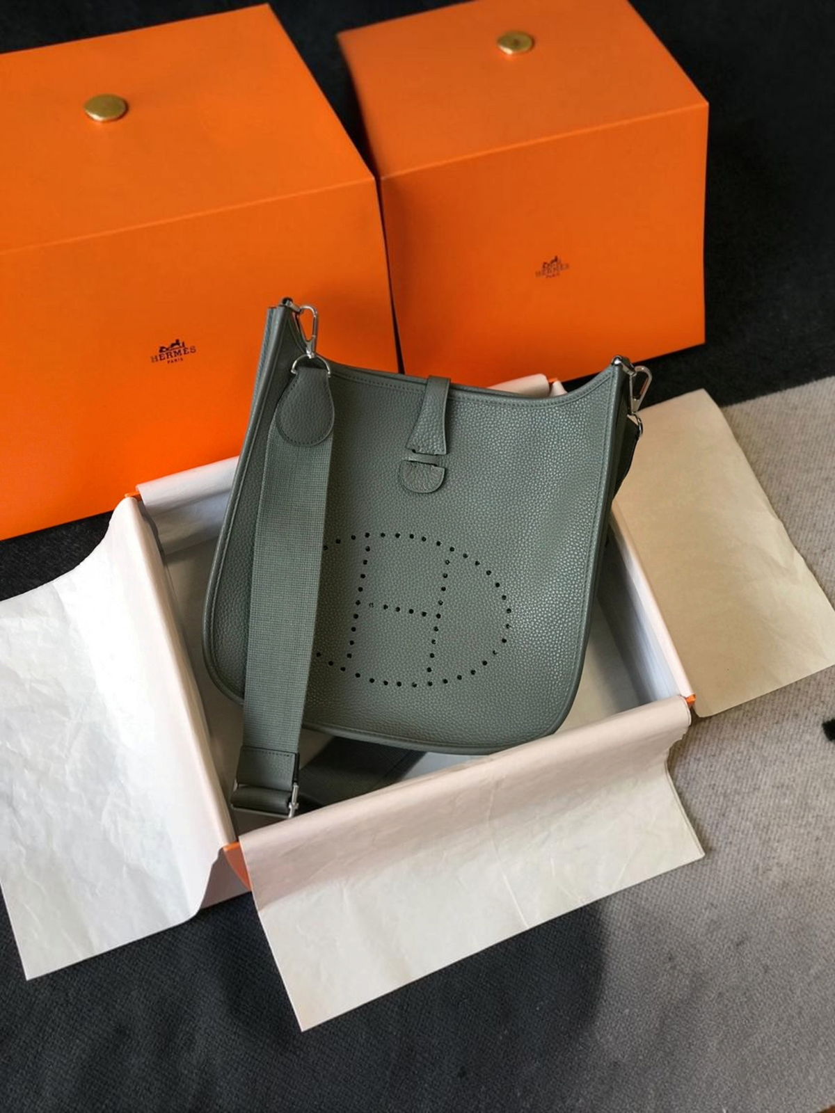 SWORD LUXURY Hermès Evelyne PM 28 gri renkli, delikli H logolu ve ayarlanabilir kanvas askılı deri çanta.