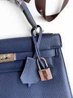 SWORD LUXURY lacivert Togo deri Kelly 25 çanta, gümüş donanımlı kilit ve ikonik el işçiliği detayları ile.