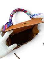 SWORD LUXURY marka, 28 cm boyutunda, taba rengi Box deri Hermès Kelly çanta, renkli twilly eşarp detaylı iç görünüm.