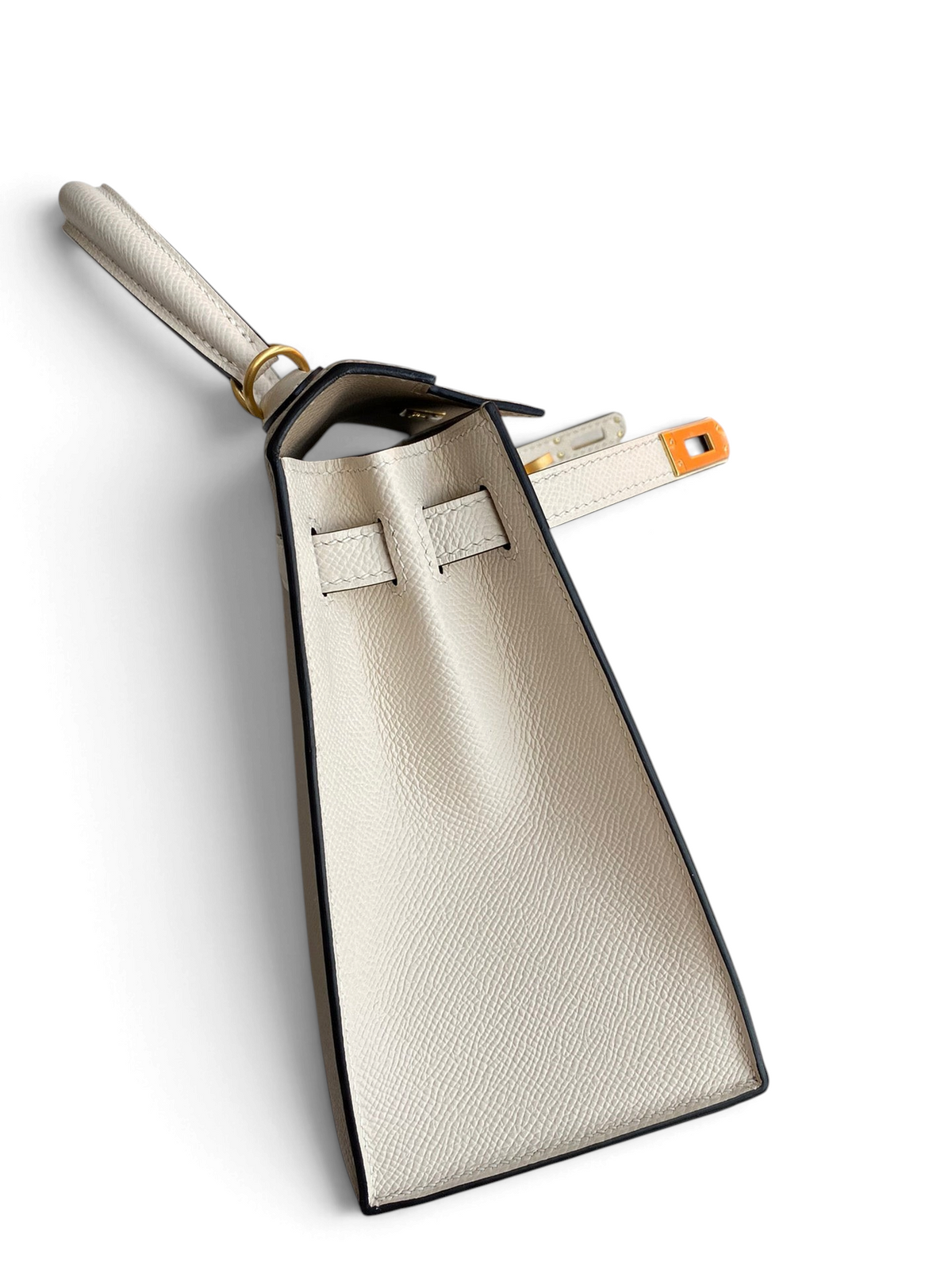 SWORD LUXURY marka, beyaz Epsom deriden üretilmiş, yan profilden görünen zarif Hermès Kelly 25 çanta.