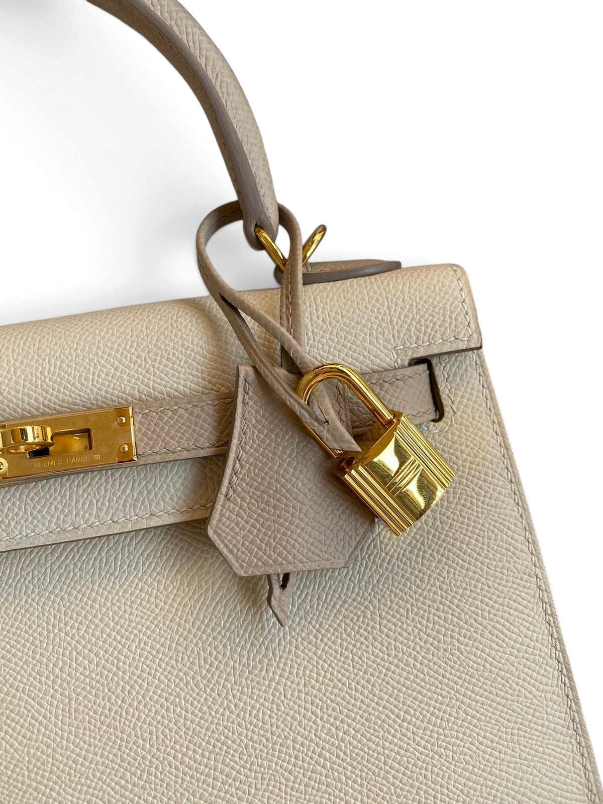 SWORD LUXURY Hermès Kelly 25 çanta, Craie ve Etoupe Epsom deri, altın donanım ve ikonik asma kilit detayı ile.