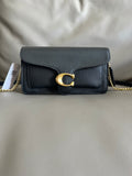 Black leather handbag with gold chain and clasp on a light gray background
