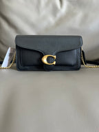 Black leather handbag with gold chain and clasp on a light gray background