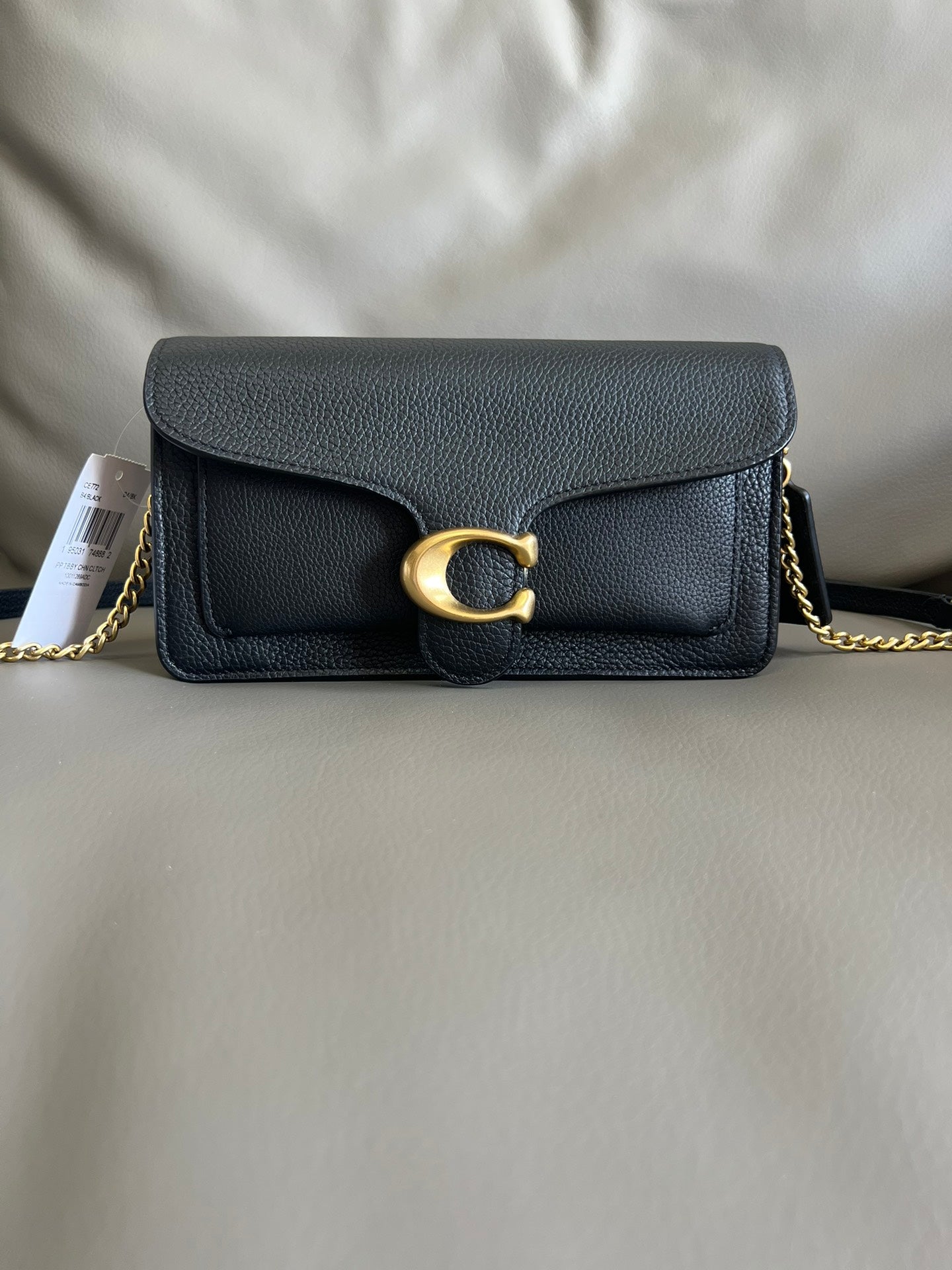 Black leather handbag with gold chain and clasp on a light gray background