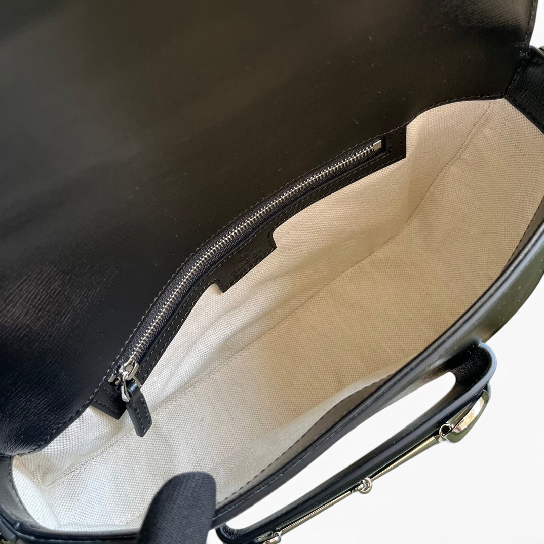 SWORD LUXURY Horsebit 1955 siyah deri omuz çantasının fermuarlı iç bölmesini ve krem rengi astarını gösteren detaylı görünüm