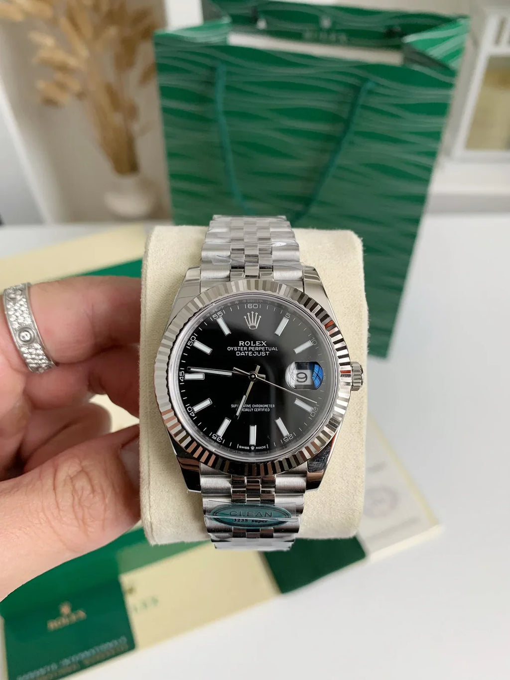 Silver watch with black face held by a hand, with a green box in the background