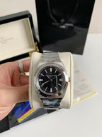 Silver watch with black face held by a hand on a light background