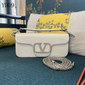 White handbag with a chain detail on a blue surface with floral cushions.