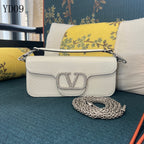 White handbag with a chain detail on a blue surface with floral cushions.