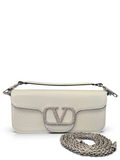 White handbag with a chain detail on a blue surface with floral cushions.