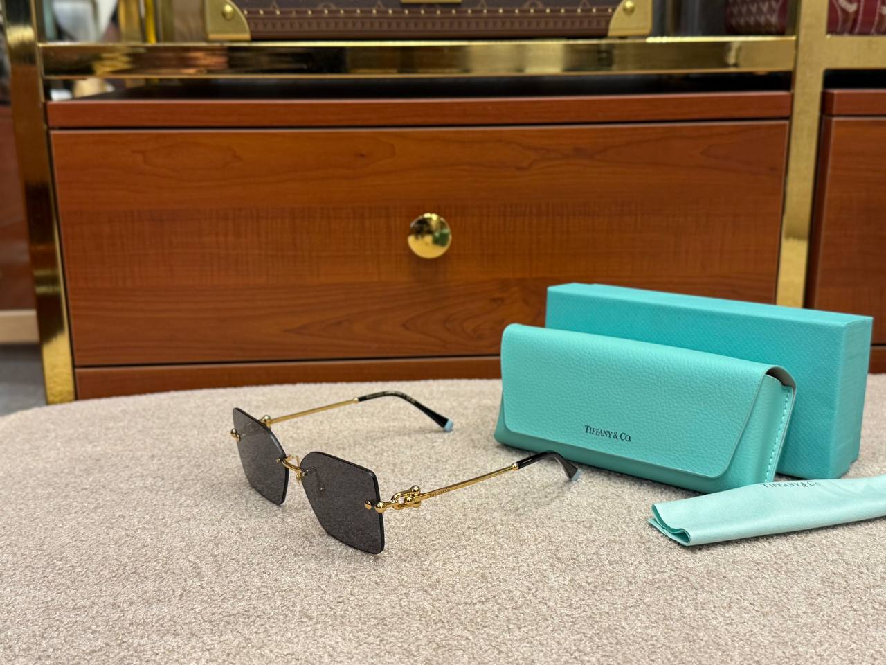 Teal sunglasses case and sunglasses on a textured surface with a wooden cabinet in the background