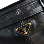 SWORD LUXURY Prada Bonnie siyah deri çanta üzerinde altın tonlu ikonik üçgen logo detayı ve kaliteli dikişler.