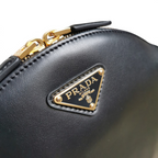 SWORD LUXURY Prada siyah deri mini omuz çantası, altın tonlu metal logo ve fermuar detaylı yakın çekim.
