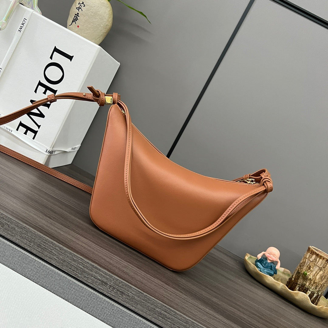 Brown leather handbag on a wooden surface with a book and decorative items in the background