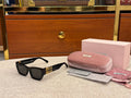 Black sunglasses with gold accents on a textured surface next to a pink case and cleaning cloth.