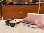 Black sunglasses with gold accents on a textured surface next to a pink case and cleaning cloth.