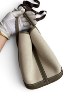 SWORD LUXURY Hermès Garden Party 30 çanta, bej kanvas ve kahverengi deri detaylı, kutusunda tutulan yan görünüm.
