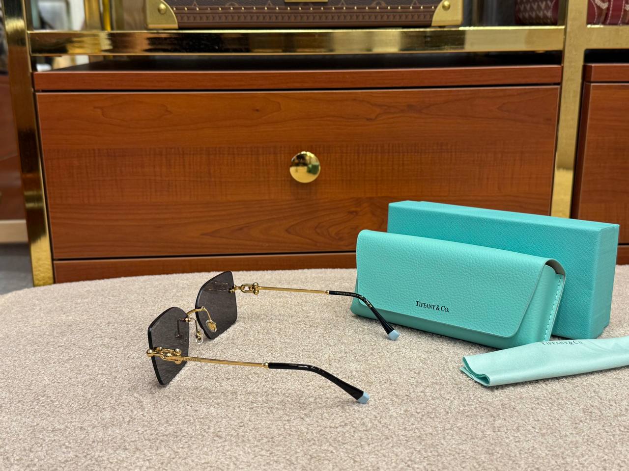 Tiffany & Co. sunglasses and turquoise case on a textured surface with wooden and gold accents in the background.