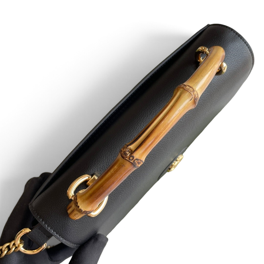 SWORD LUXURY siyah deri Gucci cüzdan, ikonik bambu sap ve altın tonlu zincir detaylarıyla kutusu üzerinde.