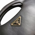 SWORD LUXURY Prada siyah deri çanta, altın tonlu üçgen logo detayı ve pürüzsüz dokusuyla yakın çekim.