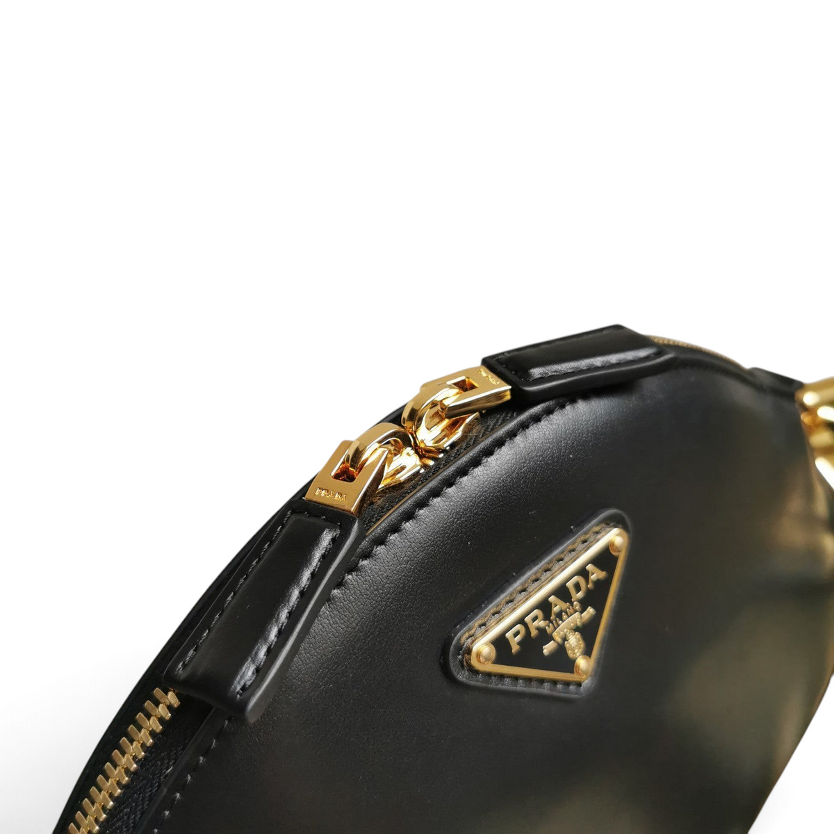 SWORD LUXURY Prada siyah deri mini omuz çantası, altın tonlu logo detayı ve fermuar aksesuarları ile yakın çekim.