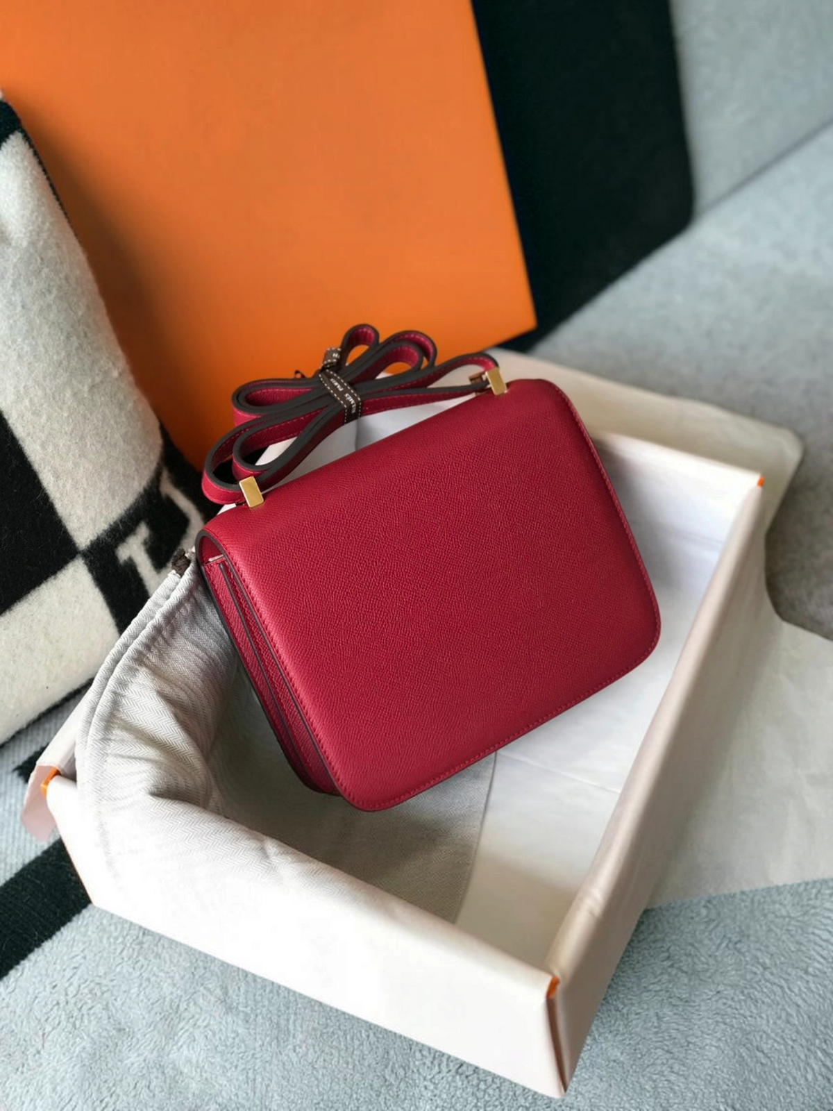 SWORD LUXURY marka, altın tonlu H tokalı, derin kırmızı deri Hermès Constance 18 çanta, kutusu ve toz torbası içinde.