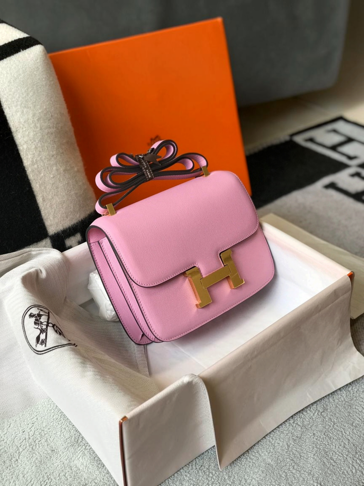 SWORD LUXURY marka, altın renkli H tokalı, açık pembe deri Hermès Constance 18 çanta, kutusu ve toz torbası içinde.