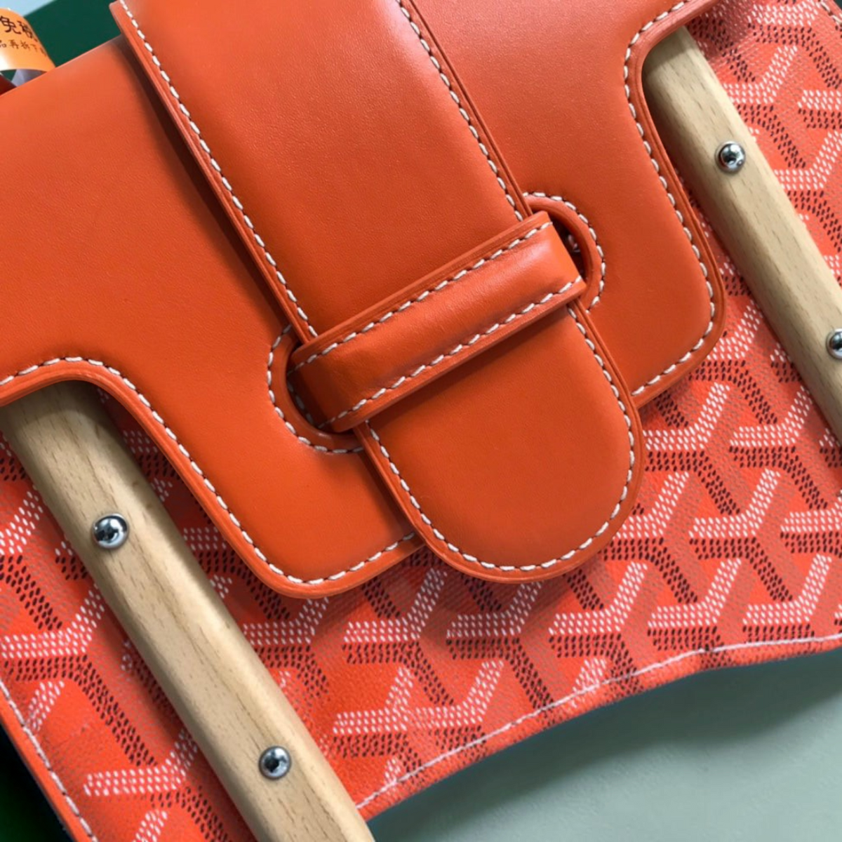 SWORD LUXURY Saïgon PM handbag featuring orange smooth leather flap with white contrast stitching and tab closure.