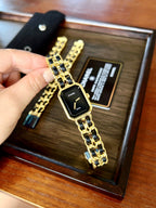 Gold and black Chanel watch on a wooden display with a hand holding it